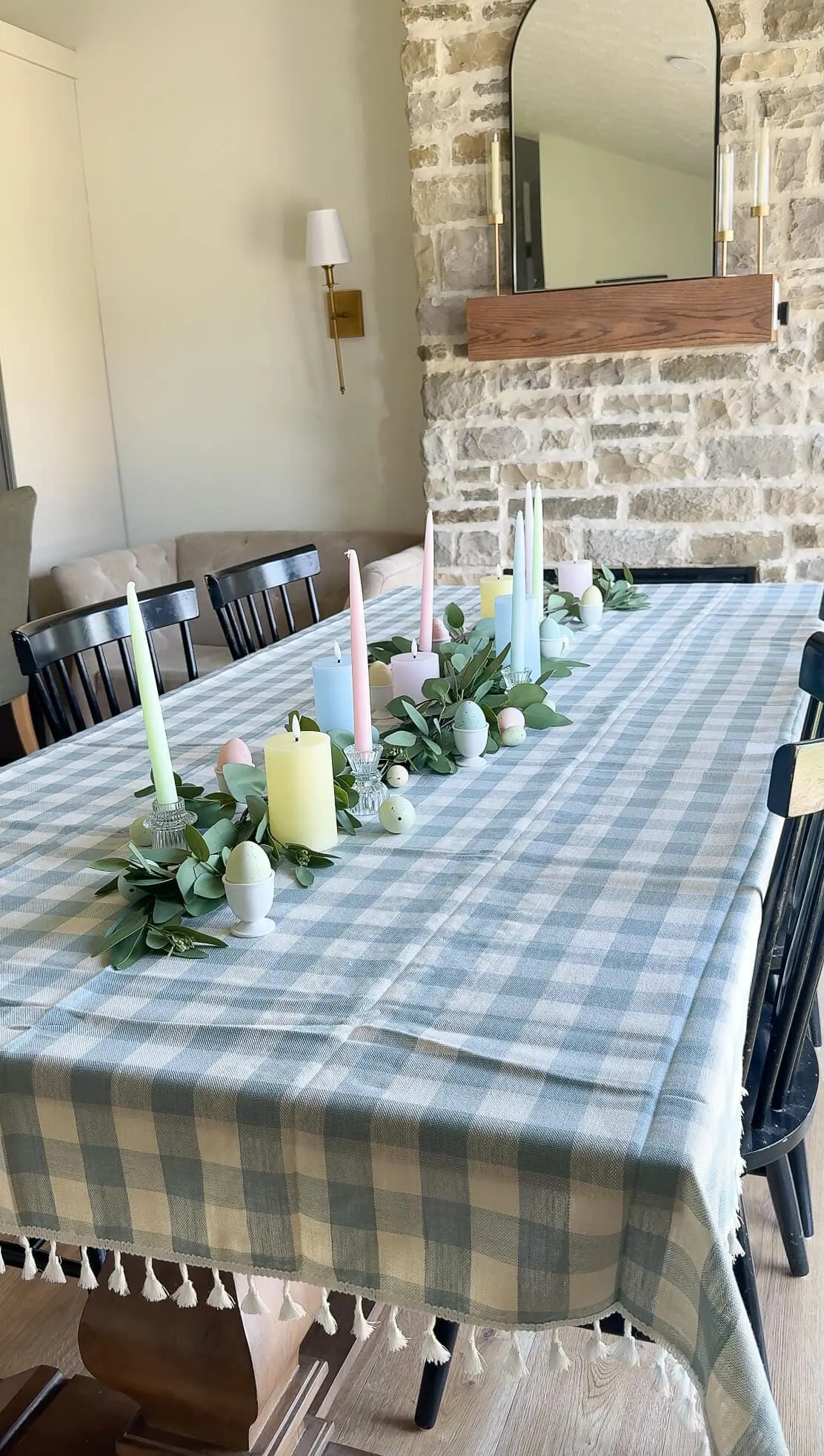 Spring tablescape featuring pastel taper candles, speckled eggs, and eucalyptus greenery on a checkered tablecloth.
